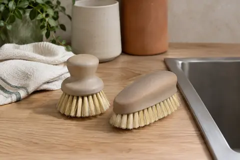 Deux brosses de vaisselle beige avec des fibres en sisal posées sur une surface en bois clair