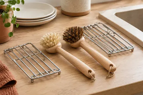 Deux brosses à vaisselle en bois et fibres végétales posées sur leurs grilles d’égouttage près d’un évier.